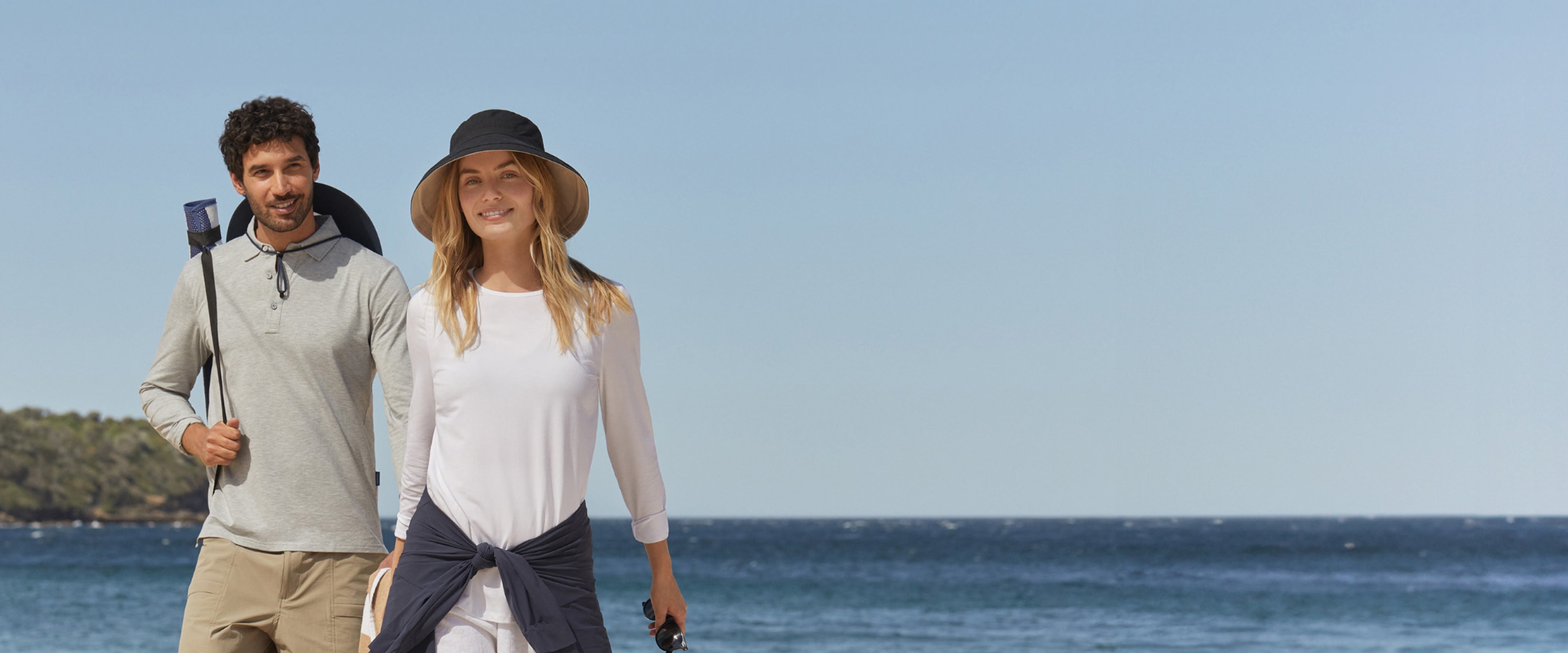 Two people walking on a beach with clear blue sky and ocean in the background