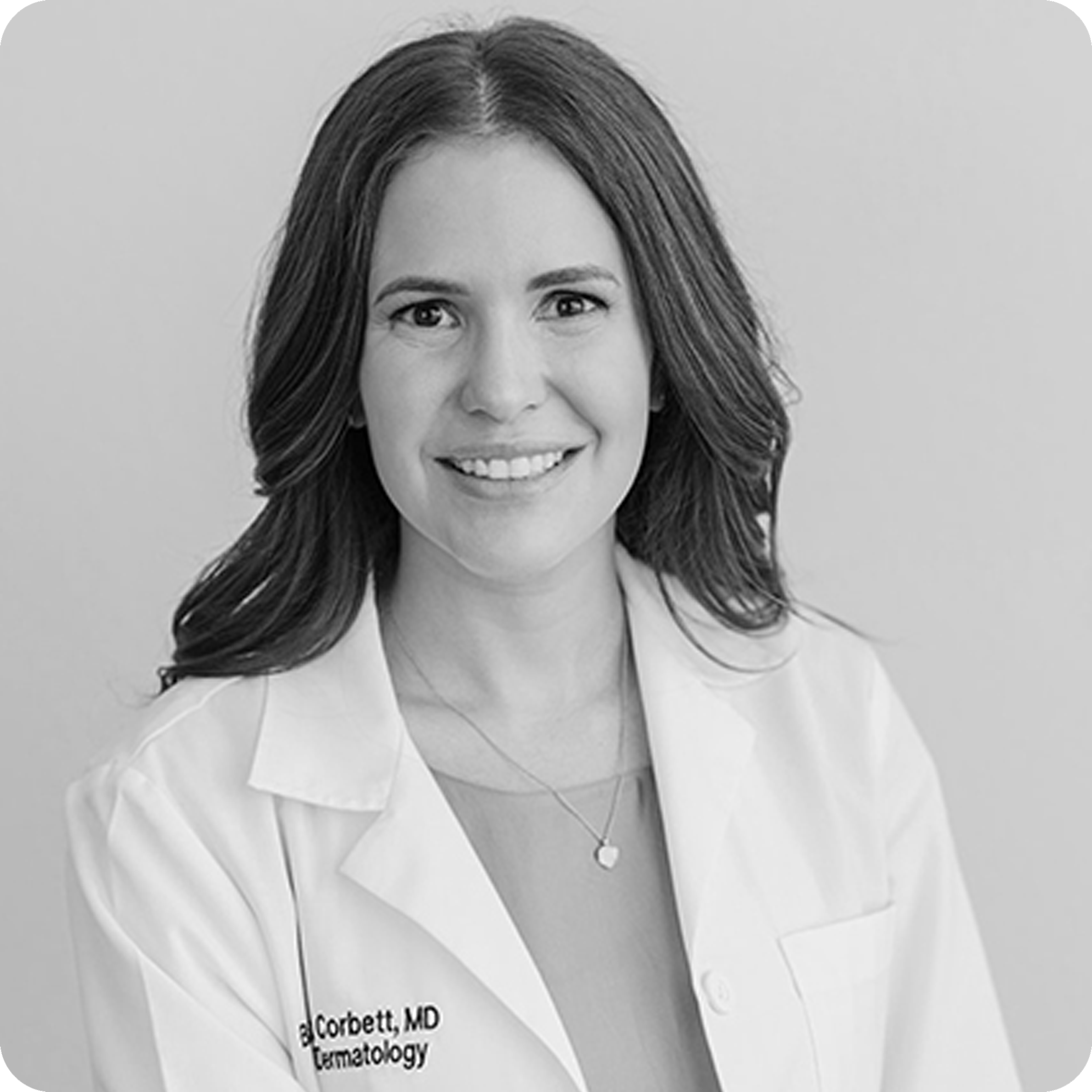 Black and white photo of a person wearing a white lab coat with a name tag.